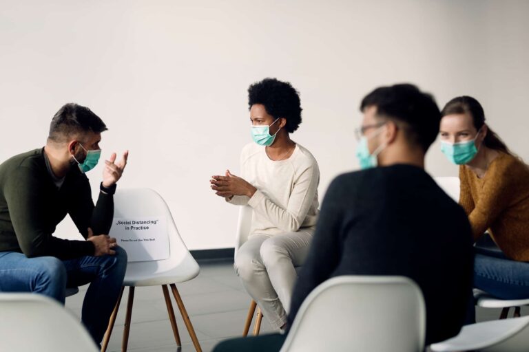 Group of people wearing protective face masks while talking during psychotherapy meeting.