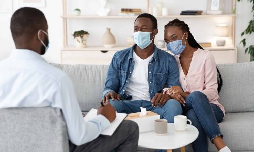 Family Therapy During Pandemic. Black Couple In Protective Masks At Counselor's Office