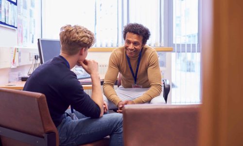 Male College Student Meeting With Campus Counselor Discussing Mental Health Issues