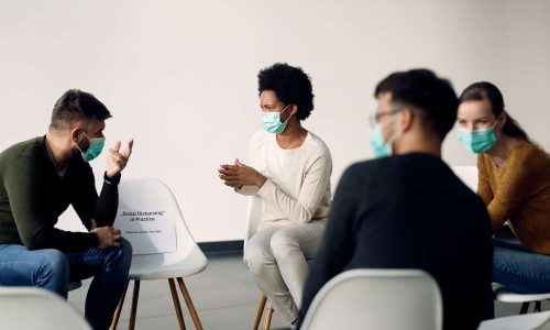 Group of people wearing protective face masks while talking during psychotherapy meeting.