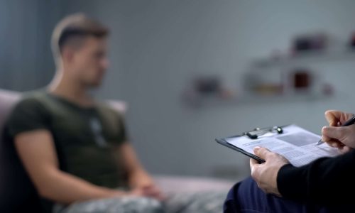 Psychologist making notes during therapy session with sad male s