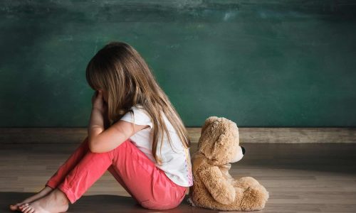 Little girl with teddy bear sitting on floor in empty room. Autism concept