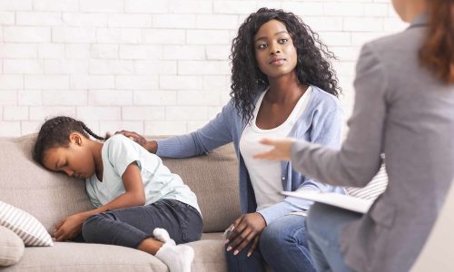 Black mom comforting her little daughter at psychologist consultation